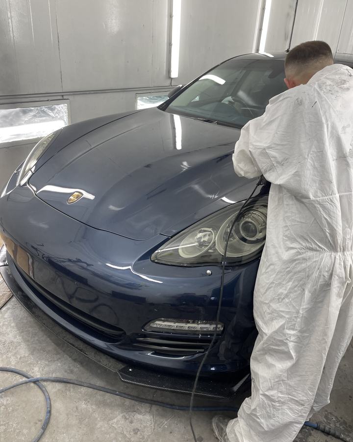 E17 Bodyworks painter in overalls checking a Porsche Panamera in the spray booth